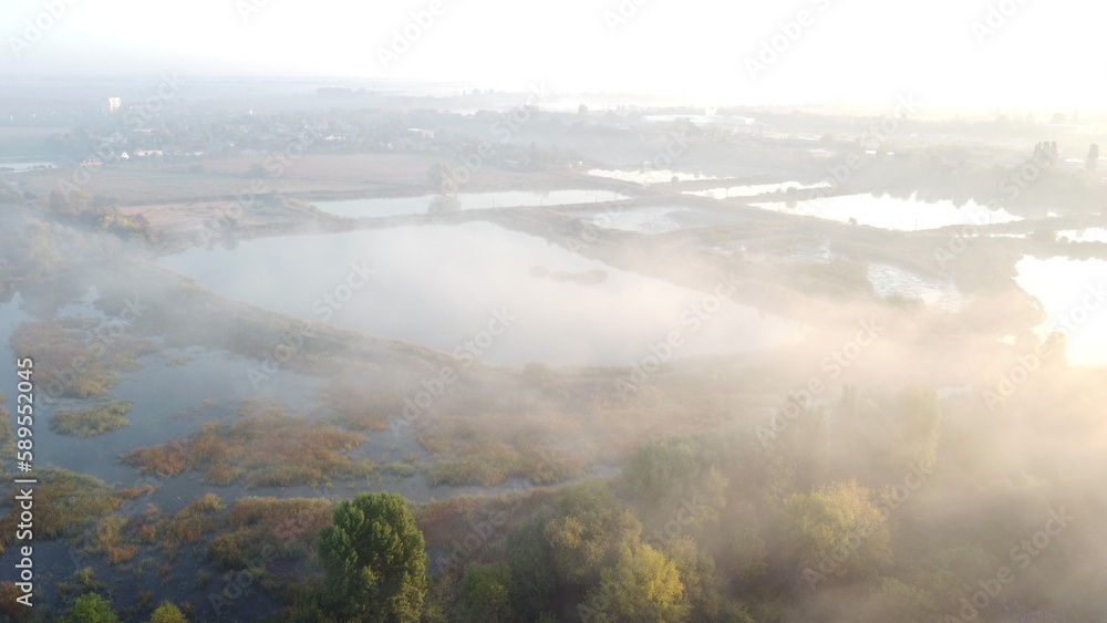 Lakes, artificially created water ponds for growing fish farming with morning mist on an early summer sunny morning. Nature scenery, natural landscape. Sunlight, sunshine. Top view. Aerial drone view.