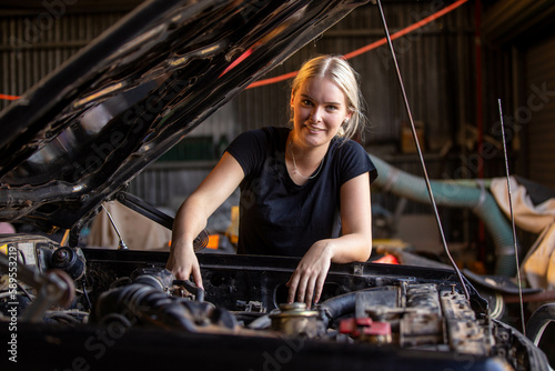 young female australian tradesperson mechanic working on car engine in auto repair garage photo