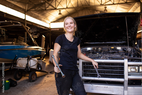 Young female aussie mechanic holding tools and leaning on a car in need of repair in workshop garage photo