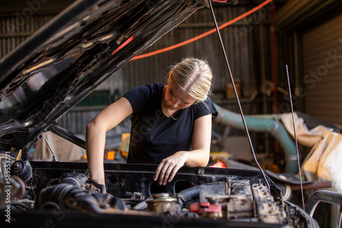 young female australian tradesperson mechanic working on car engine in auto repair garage