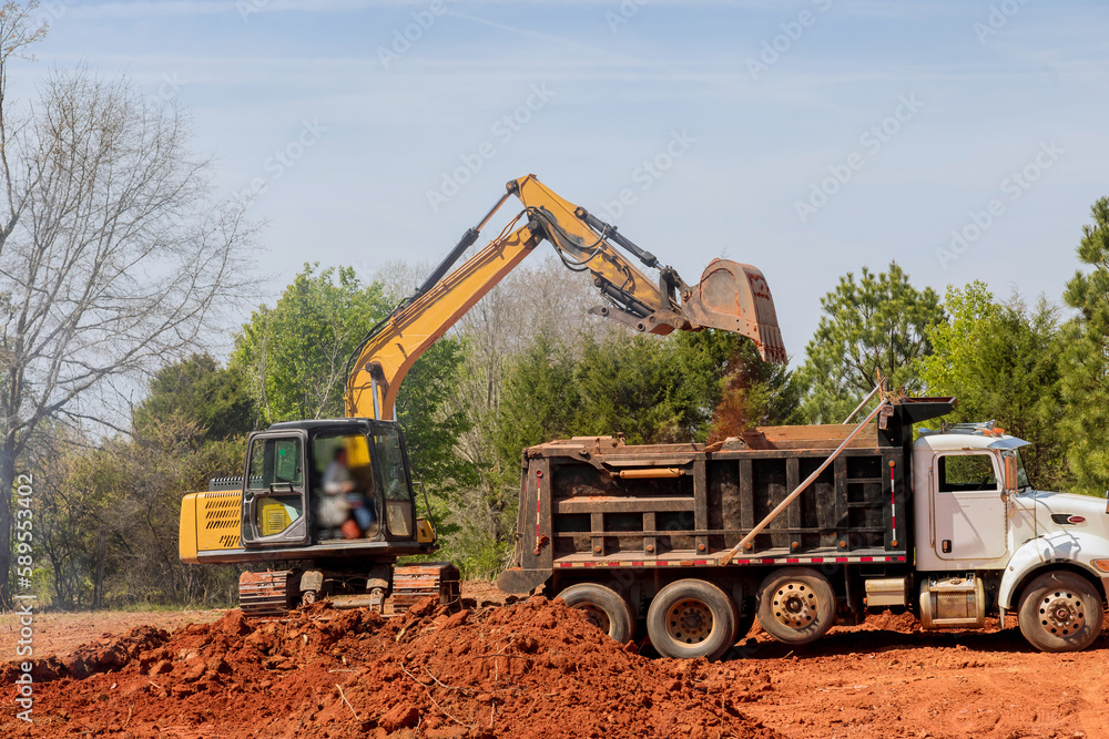 Dump truck is loading earth into an excavator on construction site Dump truck is loading earth into an excavator on construction site