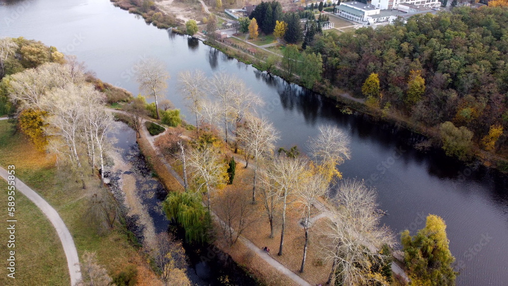 Flying over autumn park. Many trees with yellow green and fallen leaves, lakes, river, people walking along dirt paths in park on autumn day. Top view. Aerial drone view. Beautiful natural background Flying over autumn park. Many trees with yellow green and fallen leaves, lakes, river, people walking along dirt paths in park on autumn day. Top view. Aerial drone view. Beautiful natural background