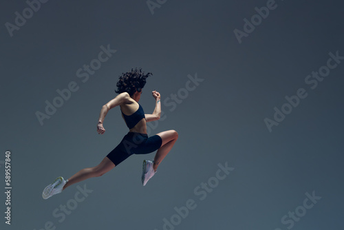 Athletic art. Dynamic image of sportive woman in motion, jumping, running, training against grey studio background. Concept of sportive lifestyle, beauty, body care, fitness, health