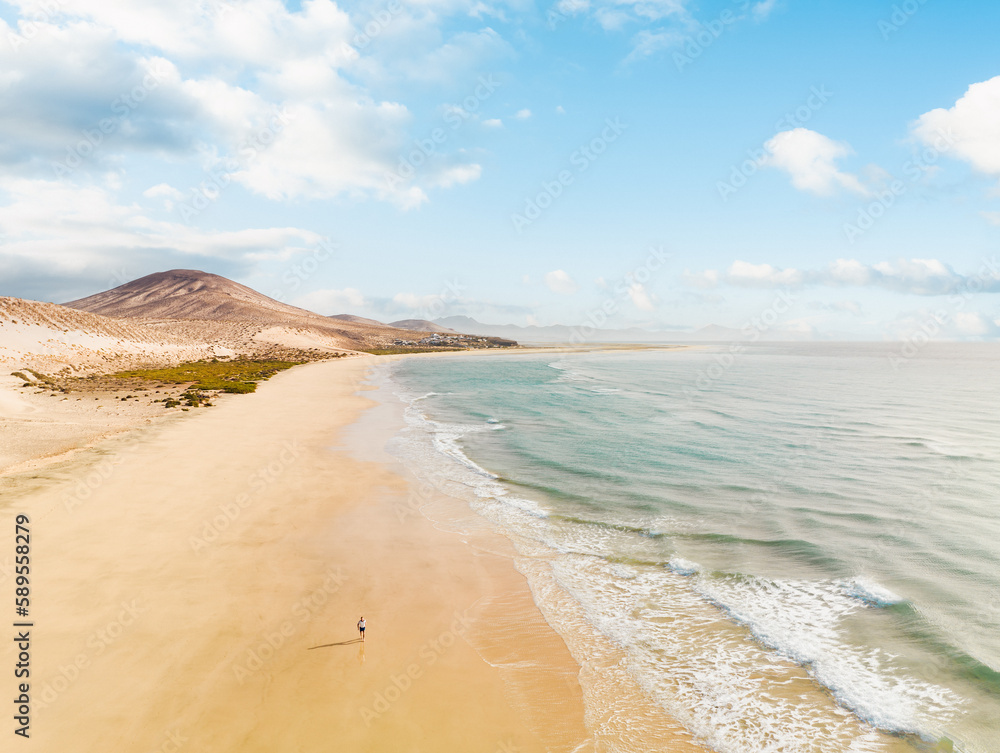 View from above, stunning aerial view of a person running on a beautiful beach bathed by the ocean and surrounded by beautiful sand dunes. Costa Calma, Fuerteventura, Canary Islands.