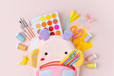 Opened kids backpack with stationery and supplies for drawing and craft on pink background. Various colorful material for creativity and art activity. Primary School or kindergarten.