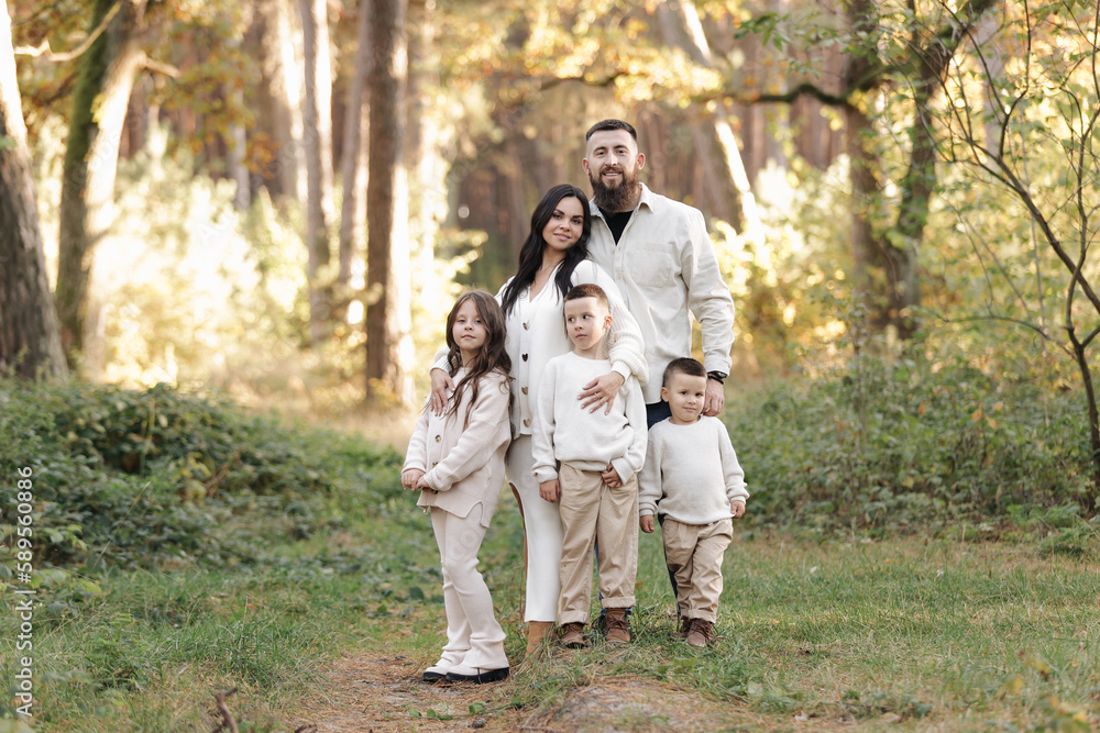 Portrait of big family outdoors. Young Stylish bearded dad with little son on shoulder, beautiful brunette mom, child boy and daughter in autumn park, smiling and looking at camera. Happy family day