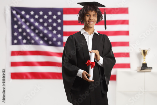 African american male student in a graduation gown holding a diploma and standing in front of USA flag photo