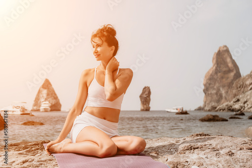 Fitness woman sea. A happy middle aged woman in white sportswear exercises morning outdoors on a beach with volcanic rocks by the sea. Female fitness pilates yoga routine concept. Healthy lifestyle.