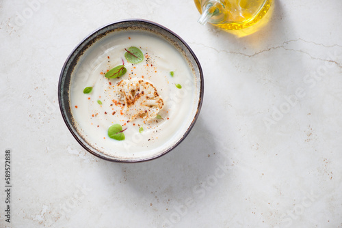 Bowl with cream-soup made of cauliflower cabbage, top view on a light-beige stone background, horizontal shot, copy space