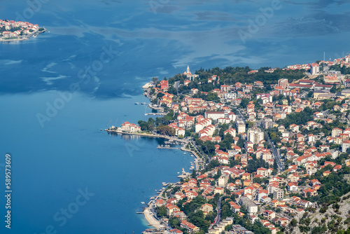 Fototapeta Naklejka Na Ścianę i Meble -  Amazing view from above of motor boats in the sky blue sea of the Bay of Kotor in Montenegro, with a picturesque coastline, red roofs of houses and the marina with boats.