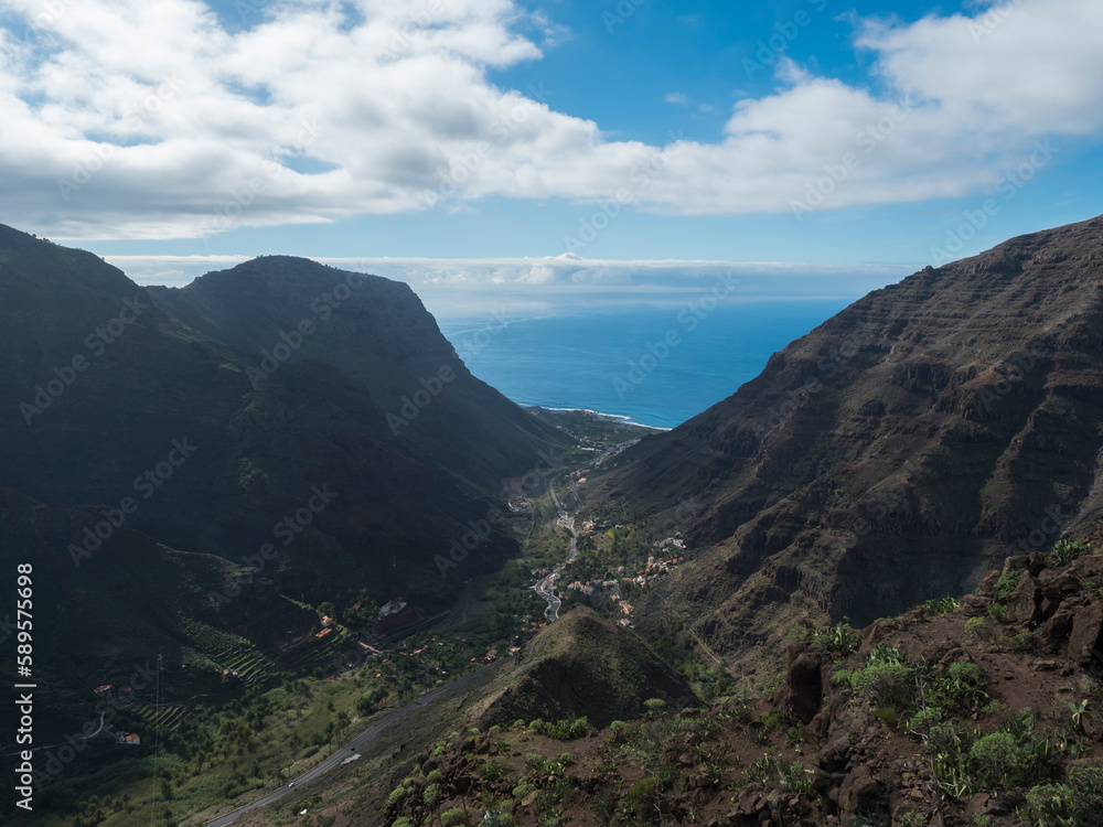 Aerial view from Mirador de Hermigua. Green valley with mountain cliffs, ocean and colorful houses village with terraced fields. La Gomera, Canary island, Spain