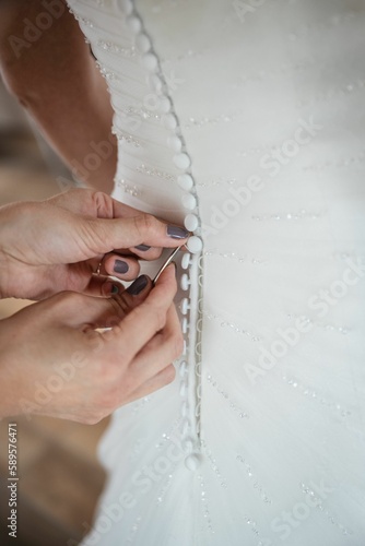 Closeup of human hands buttoning white wedding dress