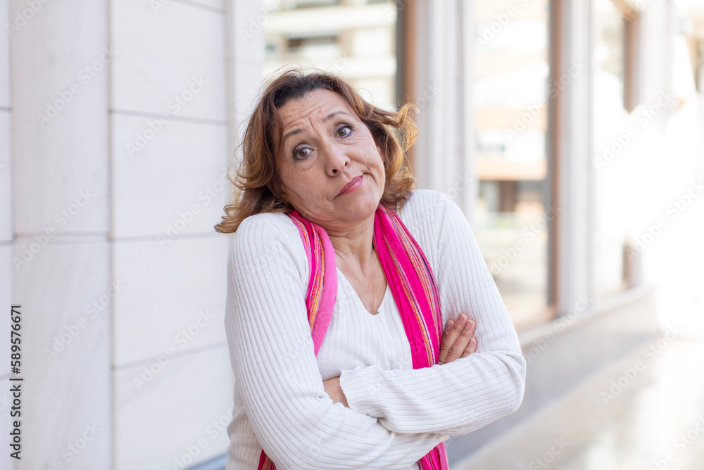 middle age woman shrugging, feeling confused and uncertain, doubting with arms crossed and puzzled look middle age woman shrugging, feeling confused and uncertain, doubting with arms crossed and puzzled look
