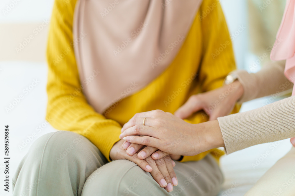 Asian muslim women encouraging her friend who have a critical problem. Woman touching and holding her friend's hands with empathy.