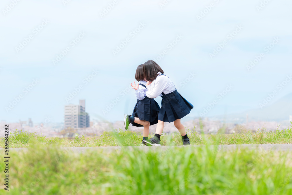 春の河川敷で遊ぶ幼稚園の制服を着た姉妹