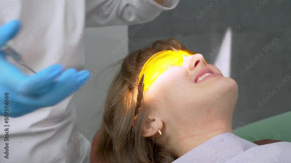 Tooth restoration with filling and polymerization lamp. Young girl