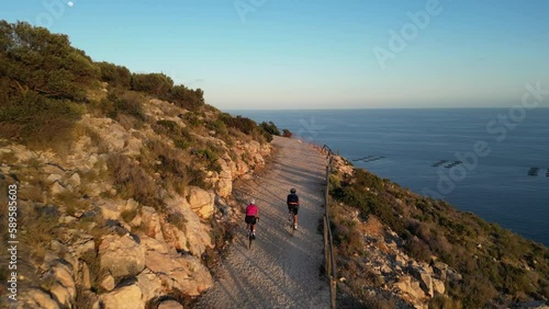 Cyclists riding on bicycle along sea.Sunset Ride.Two cyclists enjoying a scenic gravel bike adventure along an empty mountain road in Spain with stunning views of the sea.Sport motivation.Fitness.