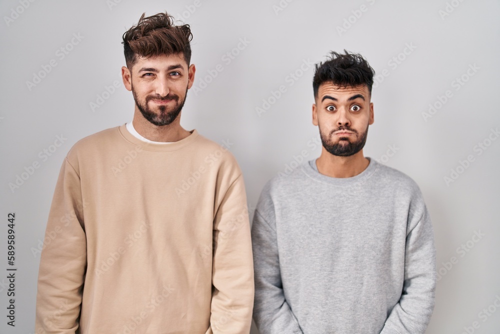 Young homosexual couple standing over white background puffing cheeks with funny face. mouth inflated with air, crazy expression. Young homosexual couple standing over white background puffing cheeks with funny face. mouth inflated with air, crazy expression.