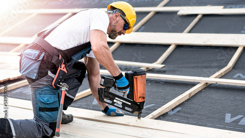 The carpenter nails a timber board using an electric nailer while working on a roof. photo