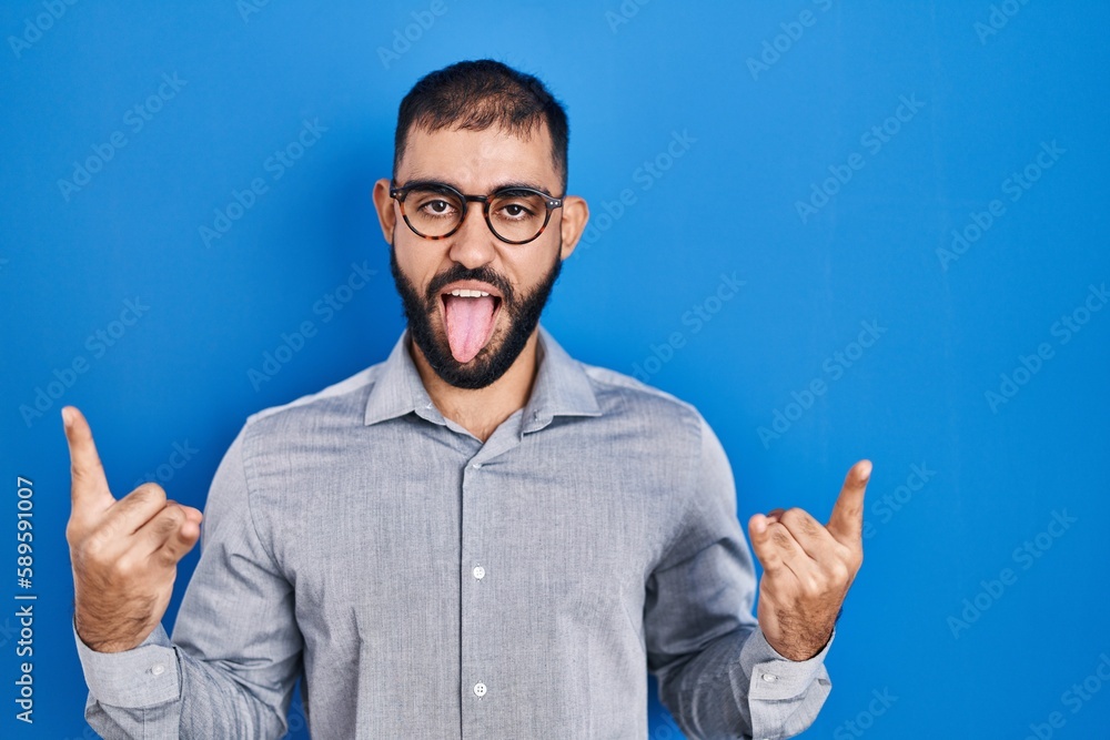 Middle east man with beard standing over blue background shouting with crazy expression doing rock symbol with hands up. music star. heavy concept. Middle east man with beard standing over blue background shouting with crazy expression doing rock symbol with hands up. music star. heavy concept.