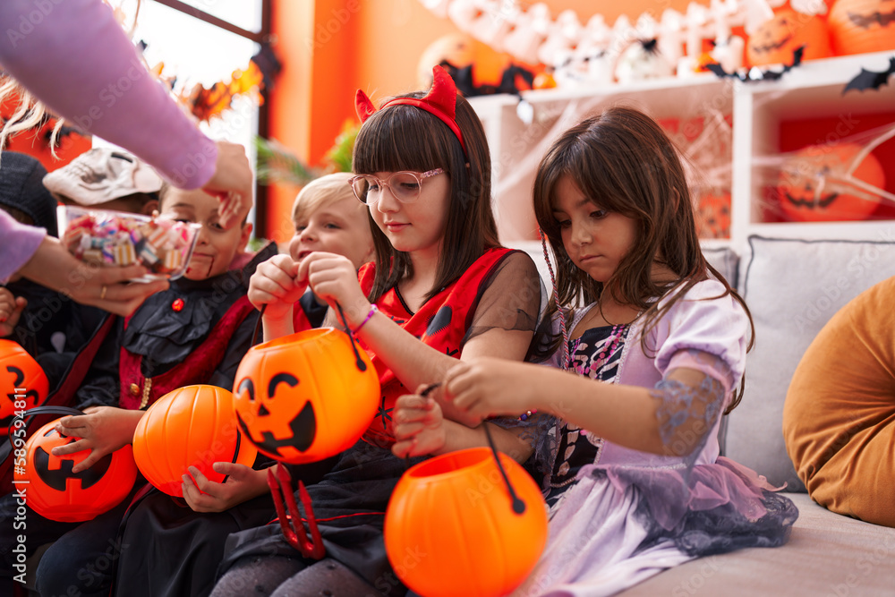 Group of kids wearing halloween costume receiving candies in pumpkin basket at home