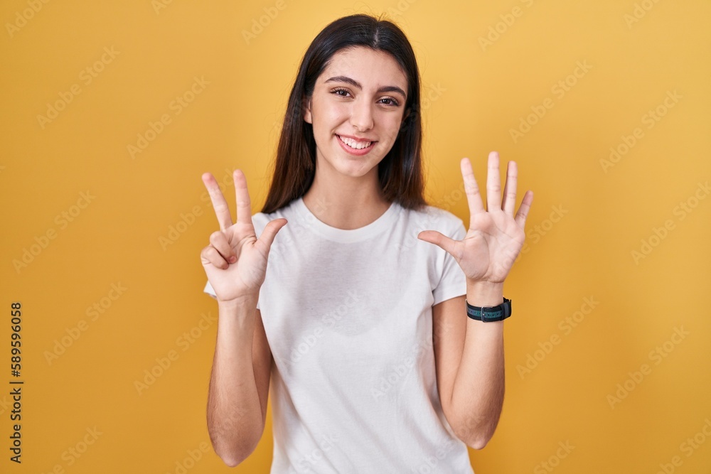 Young beautiful woman standing over yellow background showing and pointing up with fingers number eight while smiling confident and happy. Young beautiful woman standing over yellow background showing and pointing up with fingers number eight while smiling confident and happy.