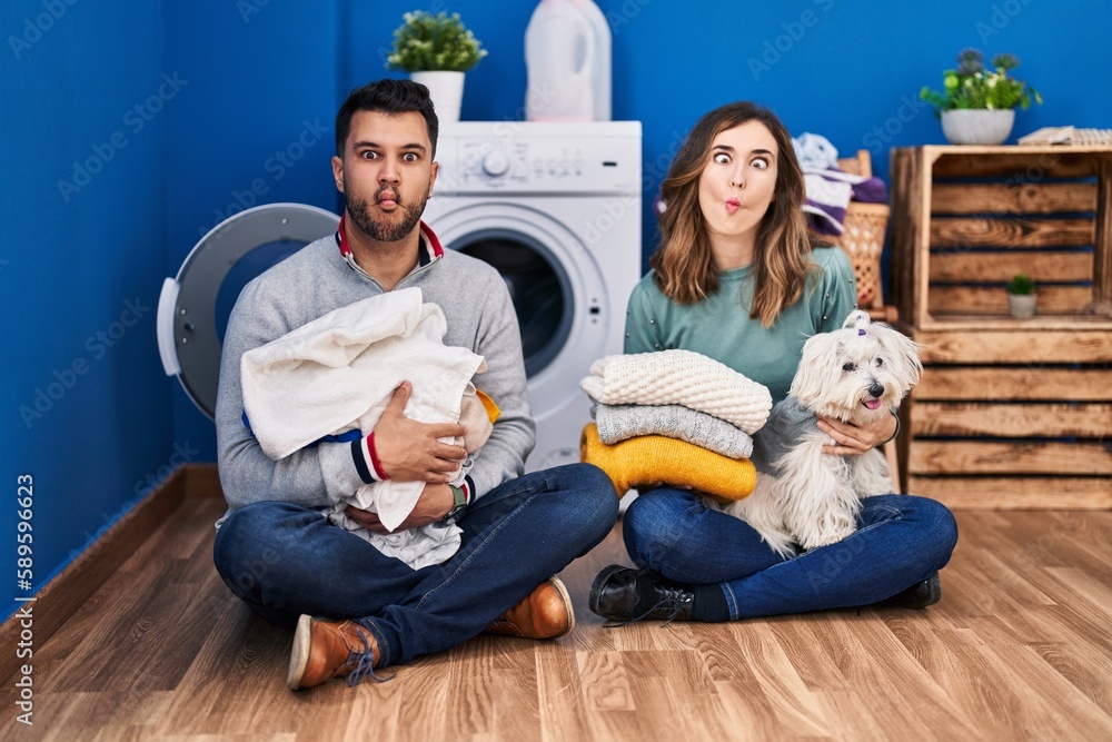 Young hispanic couple doing laundry sitting on the floor making fish face with mouth and squinting eyes, crazy and comical. Young hispanic couple doing laundry sitting on the floor making fish face with mouth and squinting eyes, crazy and comical.