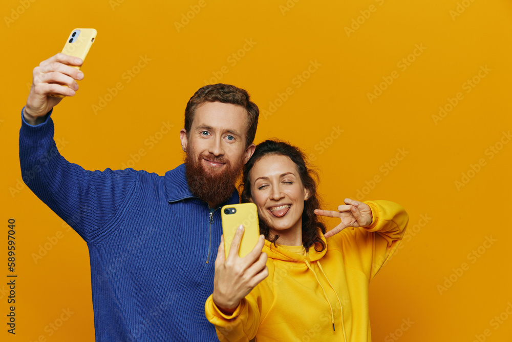 Man and woman couple smiling merrily with phone in hand social media viewing photos and videos, on yellow background, symbols signs and hand gestures, family freelancers. Man and woman couple smiling merrily with phone in hand social media viewing photos and videos, on yellow background, symbols signs and hand gestures, family freelancers.