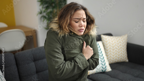 Young beautiful hispanic woman covering with jacket for cold at home