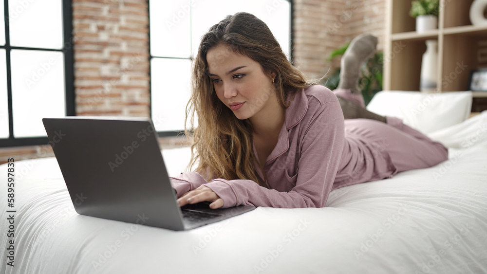 Fototapeta premium Young beautiful hispanic woman using laptop lying on bed at bedroom