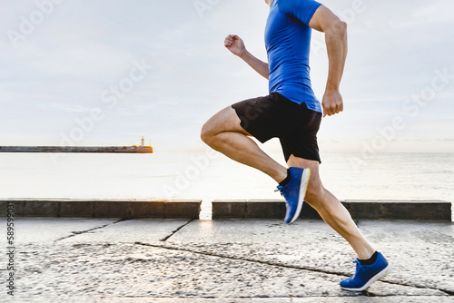 male runner running embankment in sunrise, summer jogging along seashore in background rising sun and lighthouse © sports photos