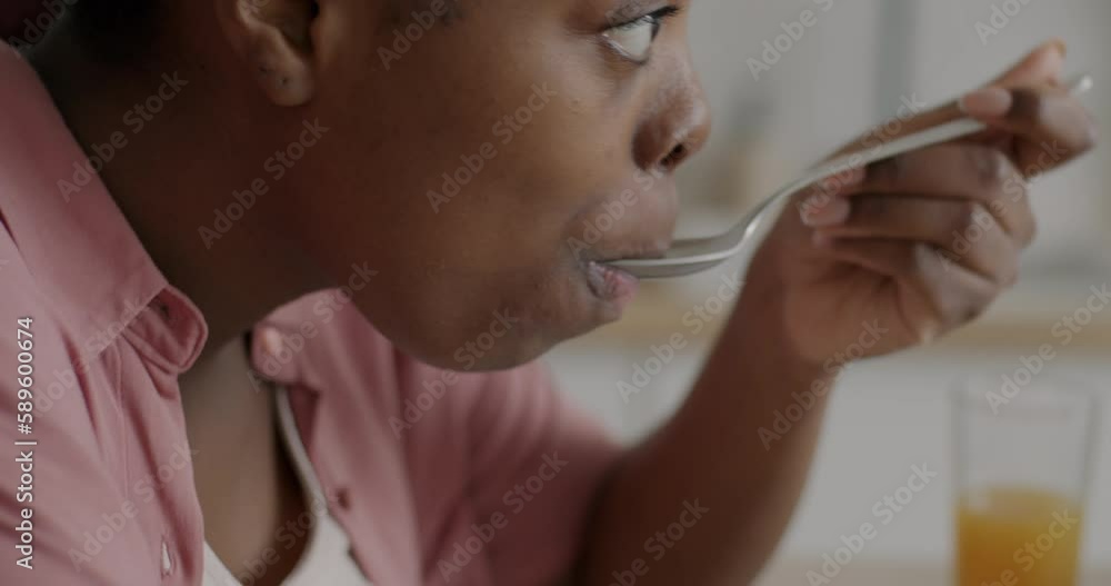 Close-up of African American woman eating cereal with milk enjoying healthy breakfast in kitchen at home. People and nutrition concept. Close-up of African American woman eating cereal with milk enjoying healthy breakfast in kitchen at home. People and nutrition concept.