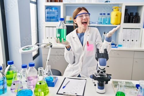 Young brunette woman working at scientist laboratory celebrating achievement with happy smile and winner expression with raised hand