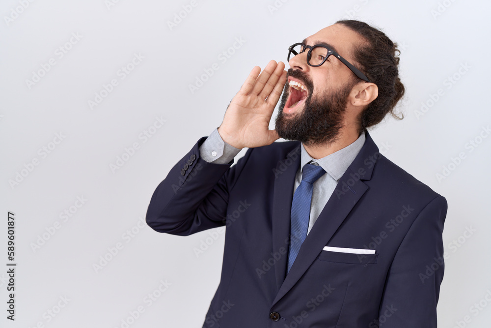 Hispanic man with beard wearing suit and tie shouting and screaming loud to side with hand on mouth. communication concept. Hispanic man with beard wearing suit and tie shouting and screaming loud to side with hand on mouth. communication concept.