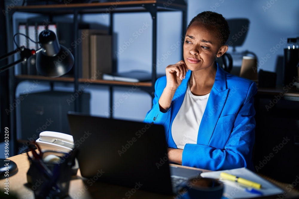Beautiful african american woman working at the office at night with hand on chin thinking about question, pensive expression. smiling with thoughtful face. doubt concept. Beautiful african american woman working at the office at night with hand on chin thinking about question, pensive expression. smiling with thoughtful face. doubt concept.