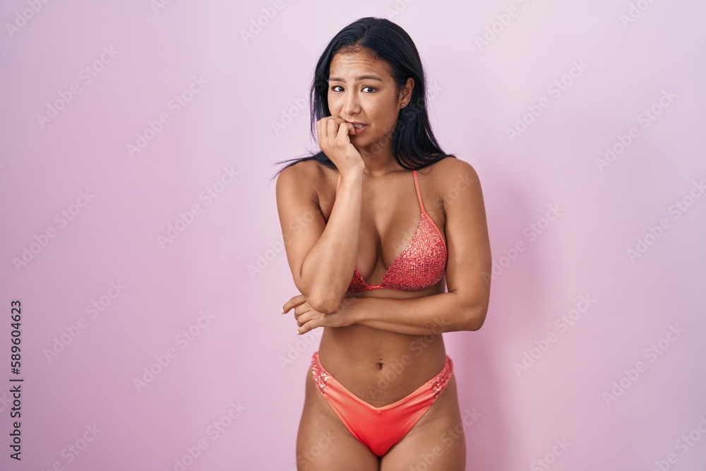 Hispanic woman wearing bikini looking stressed and nervous with hands on mouth biting nails. anxiety problem. Hispanic woman wearing bikini looking stressed and nervous with hands on mouth biting nails. anxiety problem.