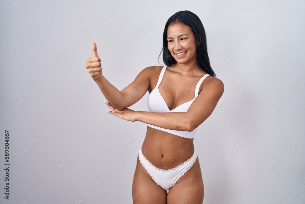 Hispanic woman wearing lingerie looking proud, smiling doing thumbs up gesture to the side Hispanic woman wearing lingerie looking proud, smiling doing thumbs up gesture to the side