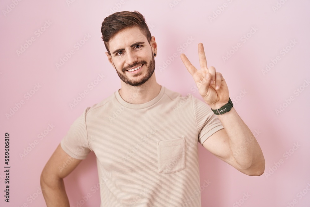 Hispanic man with beard standing over pink background smiling looking to the camera showing fingers doing victory sign. number two. Hispanic man with beard standing over pink background smiling looking to the camera showing fingers doing victory sign. number two.