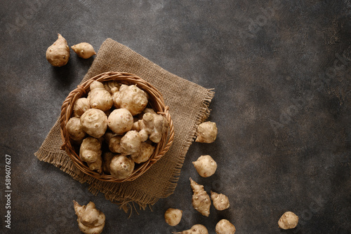 Raw Jerusalem artichoke root, sunchokes in wooden wicker basket on brown background. View from above. Copy space. photo