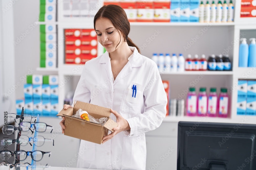 Young woman pharmacist holding package with pills at pharmacy