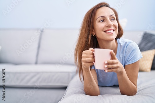 Young woman drinking coffee lying on sofa at home