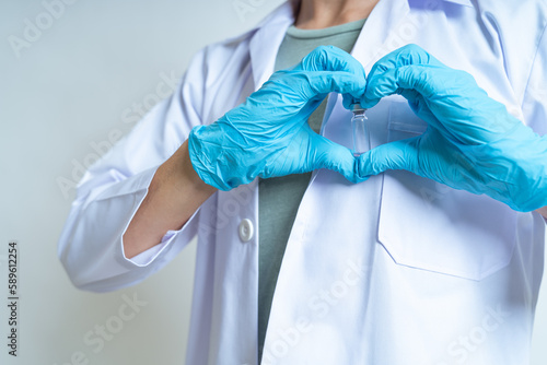 Doctor, infectionist or scientist wearing medical glove is showing coronavirus vaccine with heart sign for against coronavirus, covid-19 on white background and copy space. Covid-19 vaccine concept. photo