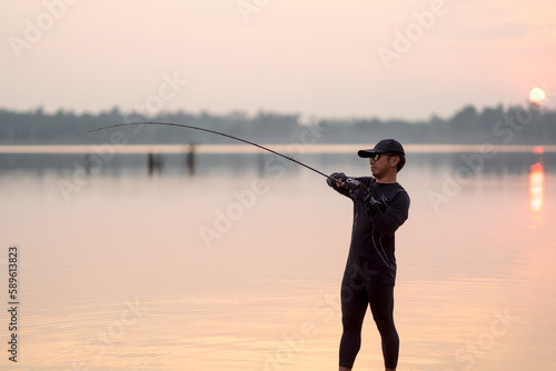 Young man fishing on a lake at sunset during the summer of the year.
