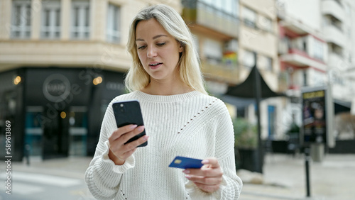 Young blonde woman shopping with smartphone and credit card at street