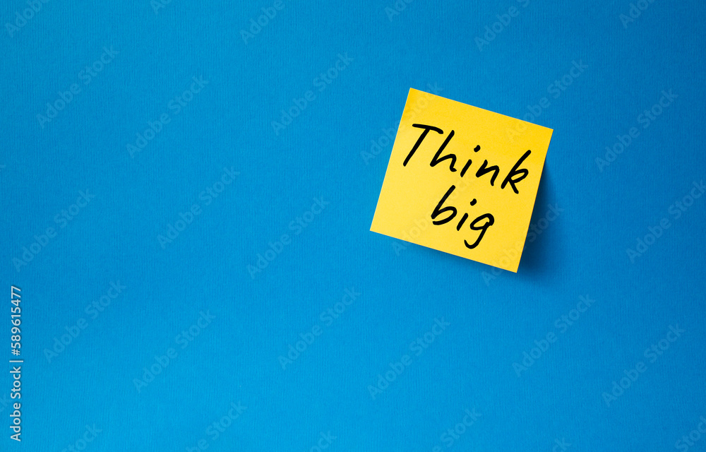 Think big symbol. Orange steaky note with words Think big. Beautiful blue background. Business and Think big concept. Copy space. Think big symbol. Orange steaky note with words Think big. Beautiful blue background. Business and Think big concept. Copy space.
