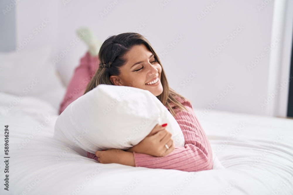 Young hispanic woman hugging pillow lying on bed at bedroom