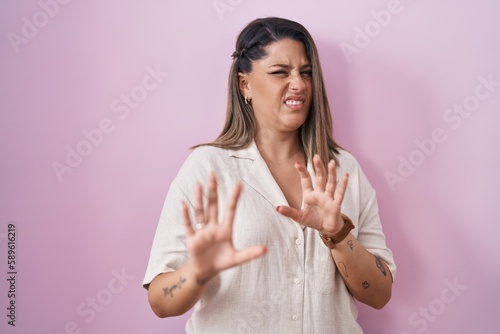 Blonde woman standing over pink background disgusted expression, displeased and fearful doing disgust face because aversion reaction.