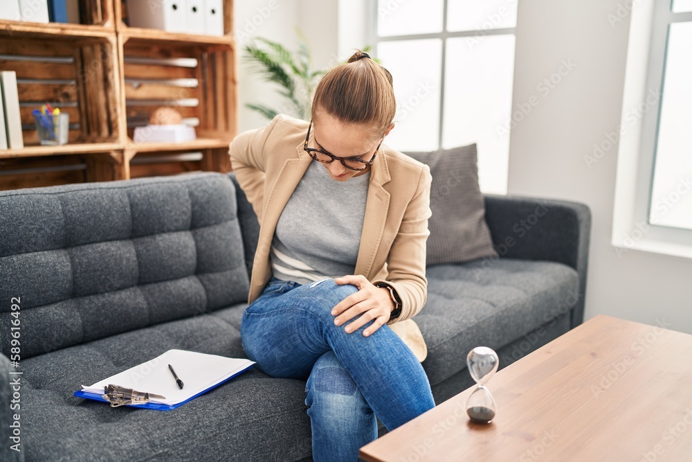 Young woman working at consultation office suffering of backache, touching back with hand, muscular pain Young woman working at consultation office suffering of backache, touching back with hand, muscular pain