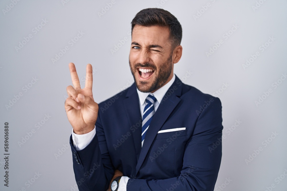 Handsome hispanic man wearing suit and tie smiling with happy face winking at the camera doing victory sign with fingers. number two. Handsome hispanic man wearing suit and tie smiling with happy face winking at the camera doing victory sign with fingers. number two.
