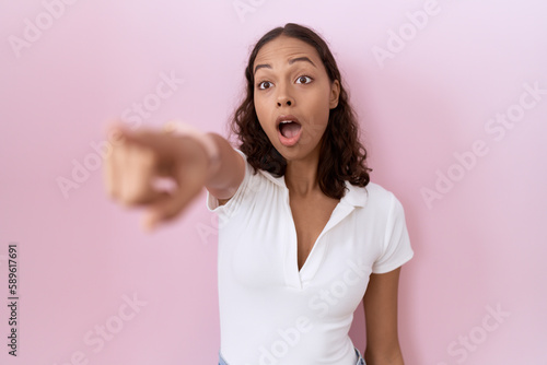 Young hispanic woman wearing casual white t shirt pointing with finger surprised ahead  open mouth amazed expression  something on the front